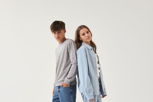 Teenie-Mädchen und Junge in lässigen Outfits von name it posieren Rücken an Rücken